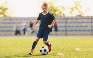 Young boy in blue soccer jersey uniform running after ball on training pitch. Kid improving dribbling skills on practice session