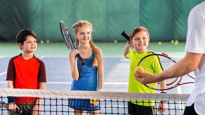 Excited children are listening to explanations of their tennis trainer with attention. They are holding rackets and laughing. Portrait