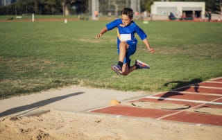 Little boy is in mid-air as he does a long jump at athletic club.