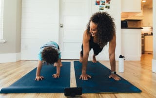 A mother exercises with her young son inside their home. She is teaching the boy the importance of a healthy lifestyle by proper stretching and exercising.