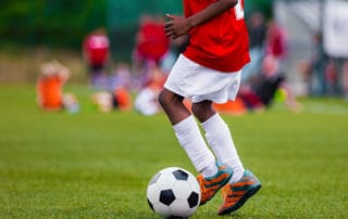 African American Boy in Junior Football Team Leading Ball on Grass Training Field. Youth Soccer Player Kicking Ball