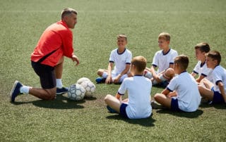 Portrait of boys sitting in front of coach on football field listening to pre game lecture