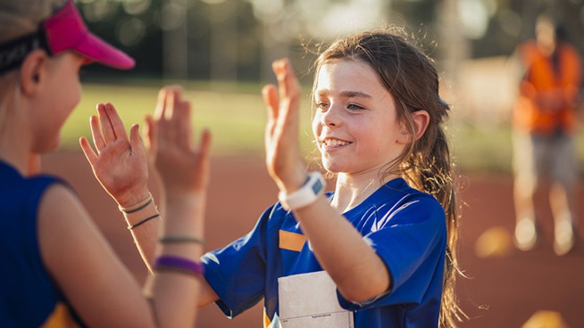 Two girls are high fiving after a difficult race in athletics club.