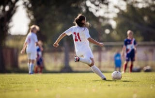 Back view of female soccer player kicking the ball during a match on a stadium.