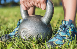 Closeup of woman's legs with sneakers in grass and hands picking up 45 pound kettlebell