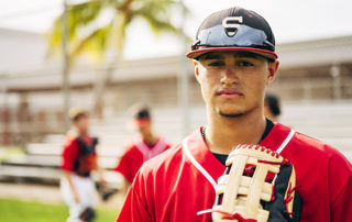 Close-up of young and serious Hispanic baseball player with glove standing outdoors and waiting for the game to begin.