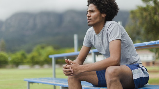 male athlete sitting on bleacher in deep thought