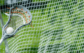 lacrosse stick in front of the net with ball in it