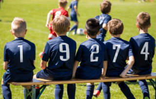 young male soccer athletes sitting on bench during a game