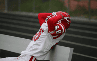 young football athlete showing frustration by grabbing helmet while sitting on bench
