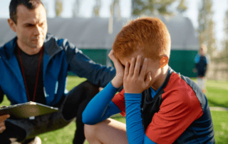 young male soccer player upset and being consoled by coach