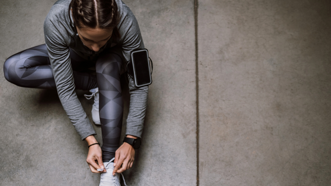 athletic woman wearing whoop wearable sports technology and tying shoe on sidewalk